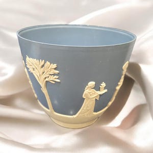 Puede incluir: Un macetero de cerámica azul con un diseño blanco de un árbol y una mujer sosteniendo una antorcha. El macetero es un diseño clásico con un acabado liso.