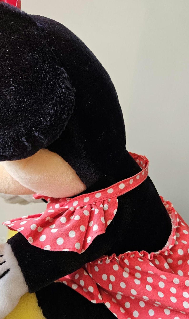 May include: A black plush toy with a red and white polka dot dress. The dress has a ruffled neckline and a white ribbon around the waist.