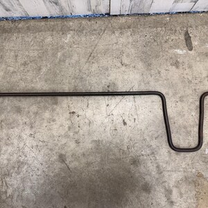Op de afbeelding: Een donkerbruine metalen wielmoersleutel. Het heeft een lange, rechte handgreep en een gebogen, U-vormig uiteinde. De sleutel heeft een afgeplatte, rechthoekige kop. Gereedschap voor het los- of vastdraaien van wielmoeren.