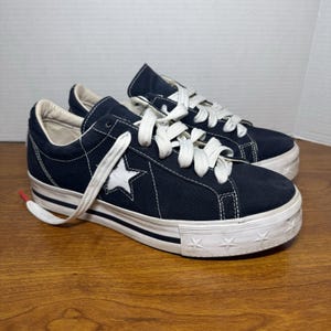 Peut inclure: Baskets en toile bleu marine avec lacets blancs et logo étoile blanc. La semelle plateforme est blanche avec une bande noire et des étoiles. Style classique et décontracté.