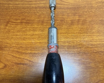 May include: A vintage hand drill with a black wooden handle, a silver metal body, and a drill bit. The drill bit is twisted and pointed. The handle is teardrop-shaped.