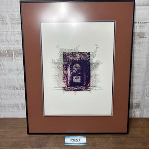 Puede incluir: Obra de arte enmarcada que presenta una ilustración detallada de una puerta arqueada con una verja de hierro forjado, rodeada de ladrillos y follaje. La obra está sobre un fondo blanco con un marco marrón y un marco negro. La palabra "POST" está en una pequeña etiqueta.