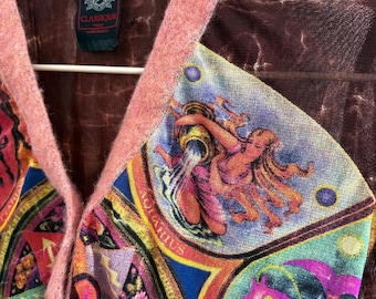 May include: A vintage, multi-colored cardigan with a unique design. The cardigan features a brown mesh body, a pink trim, and a colorful patterned front with zodiac imagery. The label reads "Jean Paul Gaultier Classique".