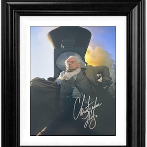 Puede incluir: Impresión enmarcada que presenta a un hombre con chaleco y bufanda, sentado en un tren. La impresión está firmada y se establece sobre un fondo de tren y cielo. Una pancarta roja en la parte superior dice "30% OFF". El marco es negro.