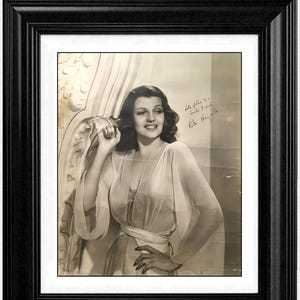 Peut inclure: Photographie vintage encadrée en noir de Rita Hayworth en robe transparente. L'image en noir et blanc porte une signature et le texte "Life is a smile...Rita Hayworth". Une bannière rouge en haut indique "30% OFF".