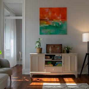 Pode incluir: Um armário branco com duas portas e uma gaveta, cheio de jogos de tabuleiro. O armário está numa sala de estar com um candeeiro de pé, um tapete e uma grande pintura abstrata na parede.