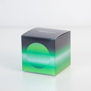 May include: A square box with a gradient design, transitioning from dark blue to green. A large green circle is centered on the front. The text "THE MORE & WHEN" is printed on the top.