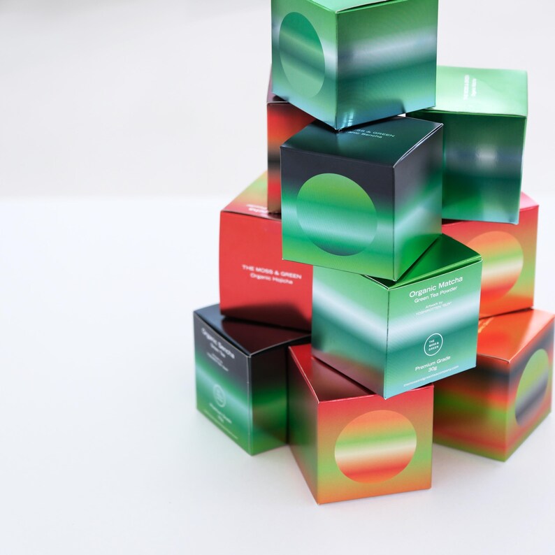 May include: A pile of square boxes with a gradient design in green, black, and red. Each box has a large, circular design. Some boxes are labelled "Organic Matcha Green Tea Powder".