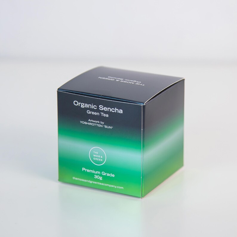 May include: A square box of Organic Sencha Green Tea. The box features a gradient design, fading from black to green. Text on the box includes "Organic Sencha Green Tea," "Artwork by YOSHIROTTEN 'SUN'," and "Premium Grade 30g."