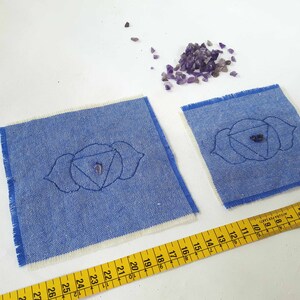 May include: Two blue fabric squares with white borders and embroidered third eye chakra symbols. The larger square measures 20 inches by 20 inches. The smaller square measures 10 inches by 10 inches. A pile of amethyst crystals is in the upper right corner of the image.