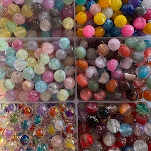 May include: A collection of colorful, round beads in various shades, including pink, yellow, blue, and orange. The beads are contained in separate compartments, showcasing their diverse colors and textures. These beads are suitable for jewelry making and crafts.