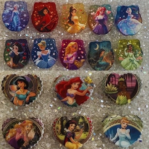May include: A collection of fourteen flat, decorative resin cabochons featuring various animated princess characters. The top two rows consist of ten scalloped-edge pieces, while the bottom row features four heart-shaped pieces with colorful illustrations.