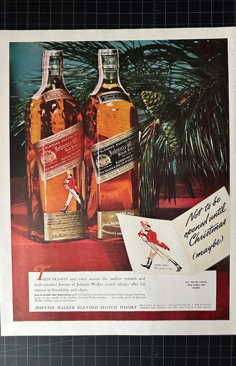 May include: Two bottles of Johnnie Walker blended Scotch whisky, one with a red label and one with a black label. The bottles are sitting on a red surface with a pine branch in the background. A small card with the text "Not to be opened until Christmas (maybe)" is in the foreground.