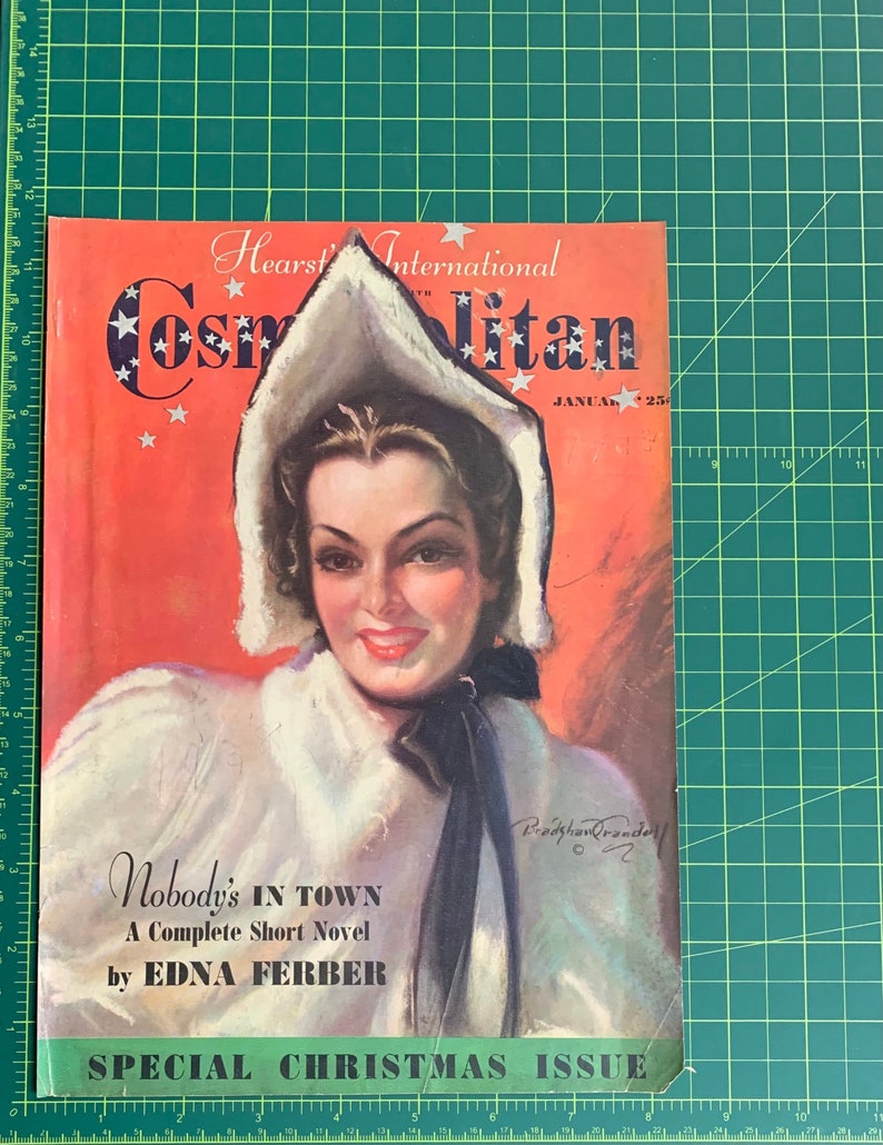 Pu&ograve; includere: Una copertina di rivista vintage con una donna che indossa un cappotto bianco con cappuccio bordato di pelliccia, con il titolo "Cosmopolitan" e il testo "Nobody's in Town, A Complete Short Novel by Edna Ferber" e "Special Christmas Issue".