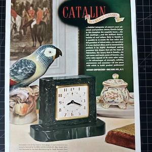 Puede incluir: Un anuncio publicitario de un reloj Catalin con una caja cuadrada de color verde oscuro con aspecto de mármol y un marco dorado. La esfera del reloj muestra la hora. El anuncio incluye texto sobre Catalin, una figura de loro y otros objetos decorativos.