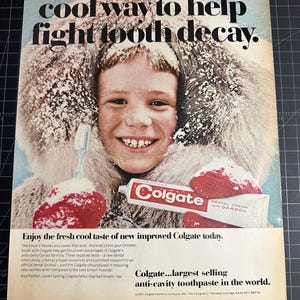 Peut inclure: Publicité vintage pour le dentifrice Colgate. Un enfant souriant, portant une capuche bordée de fourrure et des moufles rouges, tient un tube de Colgate. Le texte publicitaire dit : « C'est ici ! La nouvelle façon cool d'aider à lutter contre la carie dentaire. »