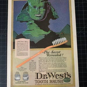 May include: A vintage advertisement for Dr. West's Tooth Brush, featuring a green sphinx with a smile. The ad claims that the brush is scientifically designed to clean teeth and massage gums. The text reads "The Secret Revealed!" and "Dr. West's Tooth Brush".