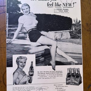 May include: Vintage black and white advertisement for Royal Crown Cola featuring Ginger Rogers. The ad includes text promoting the drink and a picture of a woman holding a bottle of RC Cola. The ad also shows a six-pack of RC Cola bottles.