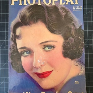May include: A vintage magazine cover featuring a woman with short, dark hair and a blue dress. The magazine is titled "PHOTOPLAY" and the cover text reads "The "NEW DEAL" In GIRLS".