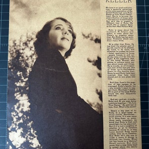 May include: Vintage black and white magazine page featuring a portrait of Ruby Keeler. The image shows a woman looking upwards with text about her career and life. The page is aged with visible wear and tear.