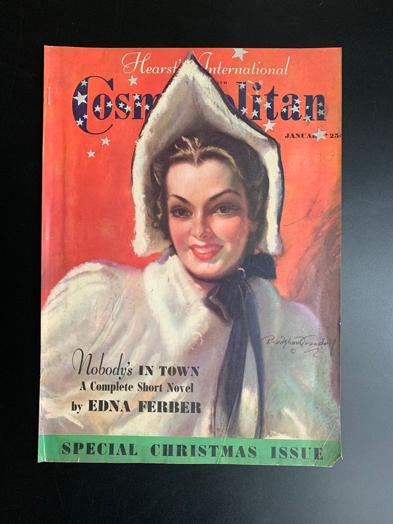 Pu&ograve; includere: Una copertina di rivista vintage con una donna in un cappotto bianco con cappuccio su uno sfondo rosso. La rivista si intitola "Cosmopolitan" e la storia di copertina &egrave; "Nobody's In Town" di Edna Ferber. La rivista &egrave; un numero speciale di Natale.