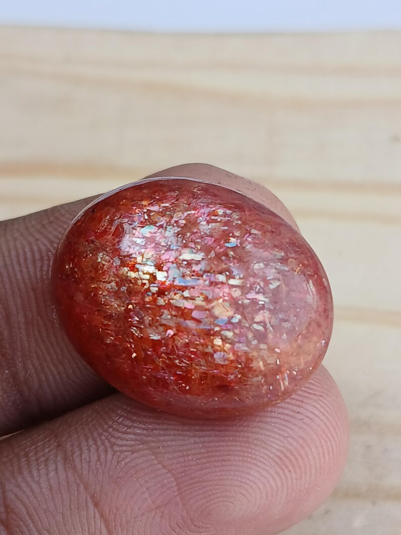 K&ouml;nnte beinhalten: Ein gro&szlig;er, ovaler Sonnenstein-Cabochon in rot-orange mit schimmerndem, irisierendem Effekt. Der Stein hat eine raue, nat&uuml;rliche Textur.