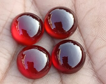 May include: Four round, glossy, red glass marbles. Each marble has a dark, reflective center and a vibrant, translucent red hue. The marbles are arranged in a square formation.