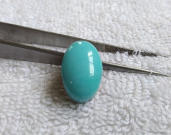 May include: A bright turquoise oval cabochon gemstone held by tweezers. The gemstone is smooth and polished.