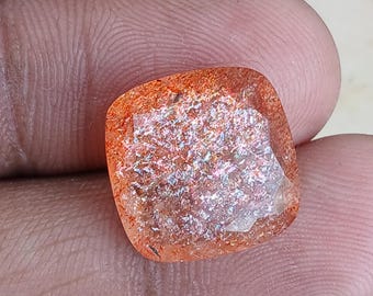 May include: A square-shaped, faceted gemstone with a reddish-orange colour and iridescent shimmer. The gemstone has a rough, natural finish.