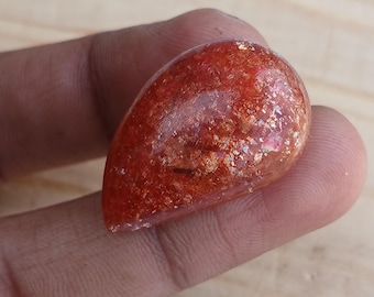 May include: A teardrop-shaped sunstone cabochon with a red-orange colour and a shimmery, iridescent finish.