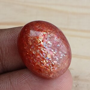 K&ouml;nnte beinhalten: Ein gro&szlig;er, ovaler Sonnenstein-Cabochon mit einer rot-orangen Basis und irisierenden Blitzen in Gold, Gr&uuml;n und Blau.