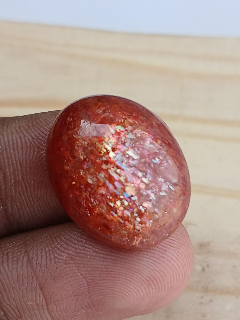 K&ouml;nnte beinhalten: Ein gro&szlig;er, ovaler Sonnenstein-Cabochon mit einer rot-orangen Basis und irisierenden Blitzen in Gold, Gr&uuml;n und Blau.
