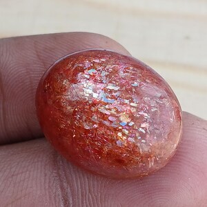 K&ouml;nnte beinhalten: Ein glatter, ovaler Sonnenstein-Cabochon in rot-orange mit irisierenden Lichtspielen.