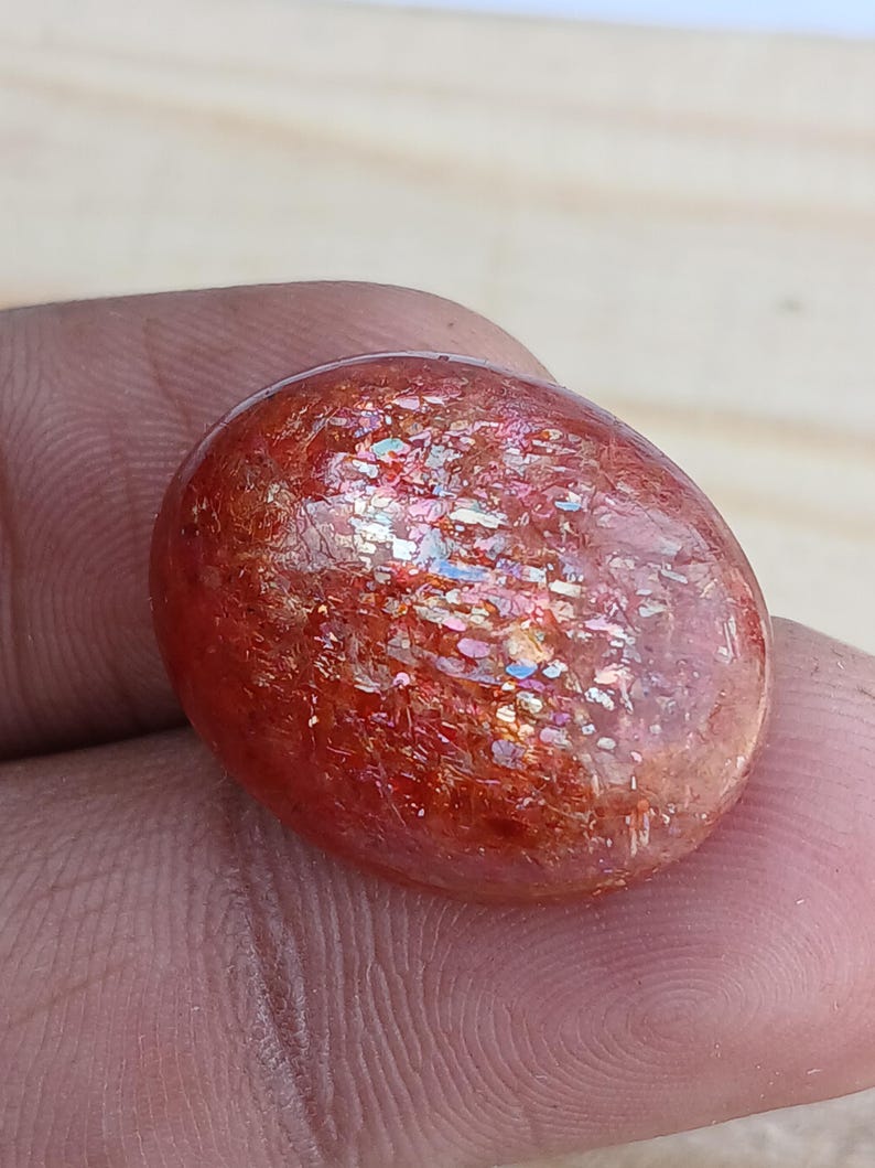 K&ouml;nnte beinhalten: Ein glatter, ovaler Sonnenstein-Cabochon in rot-orange mit irisierenden Lichtspielen.