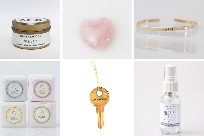 May include: A collection of self-care items including a pink heart-shaped crystal, a gold key necklace with the word "power" engraved on it, a gold bracelet with the word "Okana" engraved on it, a small candle in a gold tin with the text "Moss + Brooke Sea Salt", a bottle of pillow spray with the text "From Molly with Love Sleeping Beauty Pillow Spray", and four small bath bombs with the text "Shower Steamer" on each.