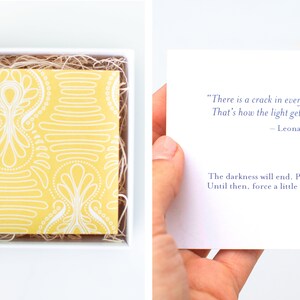 May include: A yellow and white patterned card with a quote by Leonard Cohen: "There is a crack in everything. That's how the light gets in." - Leonard Cohen. The card also includes the text: "The darkness will end. Promise. Until then, force a little light in."