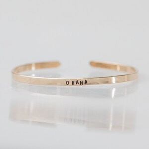 May include: A gold-toned bangle bracelet with the word "OHANA" engraved on the front.