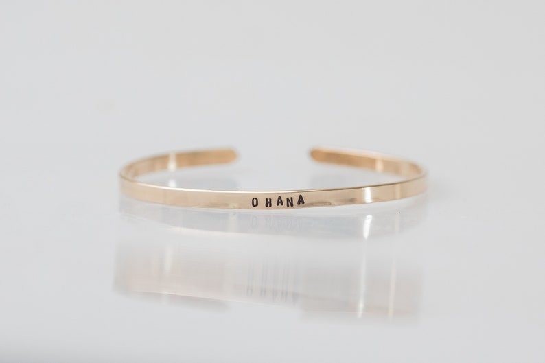 May include: A gold-toned bangle bracelet with the word "OHANA" engraved on the front.