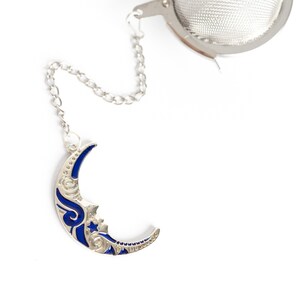 以下が含まれることがあります： 青い三日月模様の銀製のティーインフューザー。インフューザーにはチェーンと丸いメッシュボールが付いています。