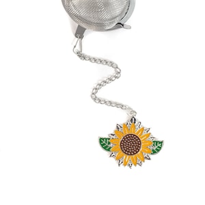 以下が含まれることがあります： チェーンとひまわりチャームが付いたシルバーのティーインフューザー。インフューザーは丸型で、メッシュデザイン。ひまわりチャームは黄色で、緑の葉が付いている。