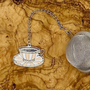 以下が含まれることがあります： チェーンと装飾的なティーカップチャームが付いたシルバーのティーインフューザー。ティーカップはピンクと白のストライプが入ったホワイトです。