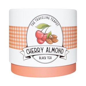 May include: A cylindrical tea container with a white label featuring an orange gingham band. The label displays a cherry and almond illustration, the text THE TRAVELING TEAPOT, CHERRY ALMOND, and BLACK TEA. The base of the container is solid orange.