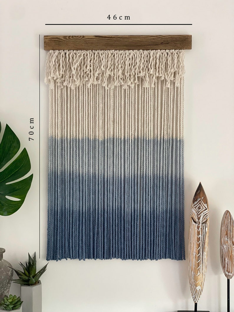 May include: A blue and white ombre macrame wall hanging with a wooden dowel at the top. The hanging measures 46 cm wide and 70 cm long.