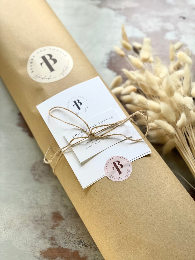 May include: A brown paper package wrapped with twine and a white card with the text "Bourne and Thread" and a logo with the letter "B". The package is decorated with two round stickers with the same logo.