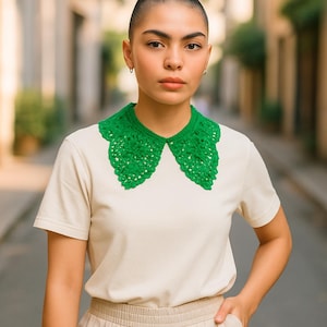 May include: A bright green, crocheted collar is the focal point of this image. The collar is worn over a cream-colored t-shirt. The collar has a scalloped edge and a detailed, open weave design. The person in the image is wearing a simple outfit.