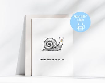 May include: A framed print featuring a whimsical illustration of a snail wearing a crown. The black and white drawing is accompanied by the text "Better late than never...." A light blue circle with the words "Printable Card" and a printer icon is in the upper right corner.
