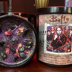 Könnte beinhalten: Eine schwarze Kerze mit einer lila Glitzeroberfläche, verziert mit schwarzen Steinen und getrockneten Blütenblättern. Das Etikett der Kerze zeigt Charaktere aus "Buffy the Vampire Slayer" und den Text "Dragon's Blood Incense".