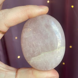 May include: A smooth, pale pink rose quartz heart-shaped stone. The stone is polished and has a light, translucent appearance.