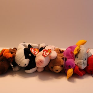 May include: A collection of nine colourful beanie baby plush toys, including a green frog, a brown moose, a black and white cow, a pink pig, a brown bear, a purple bird, a grey dolphin, a red lobster, and a yellow chick. Each toy has a red Ty tag attached.