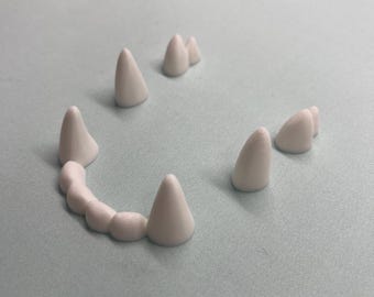 May include: A set of white plastic teeth, including a set of fangs and individual teeth, on a light blue background.